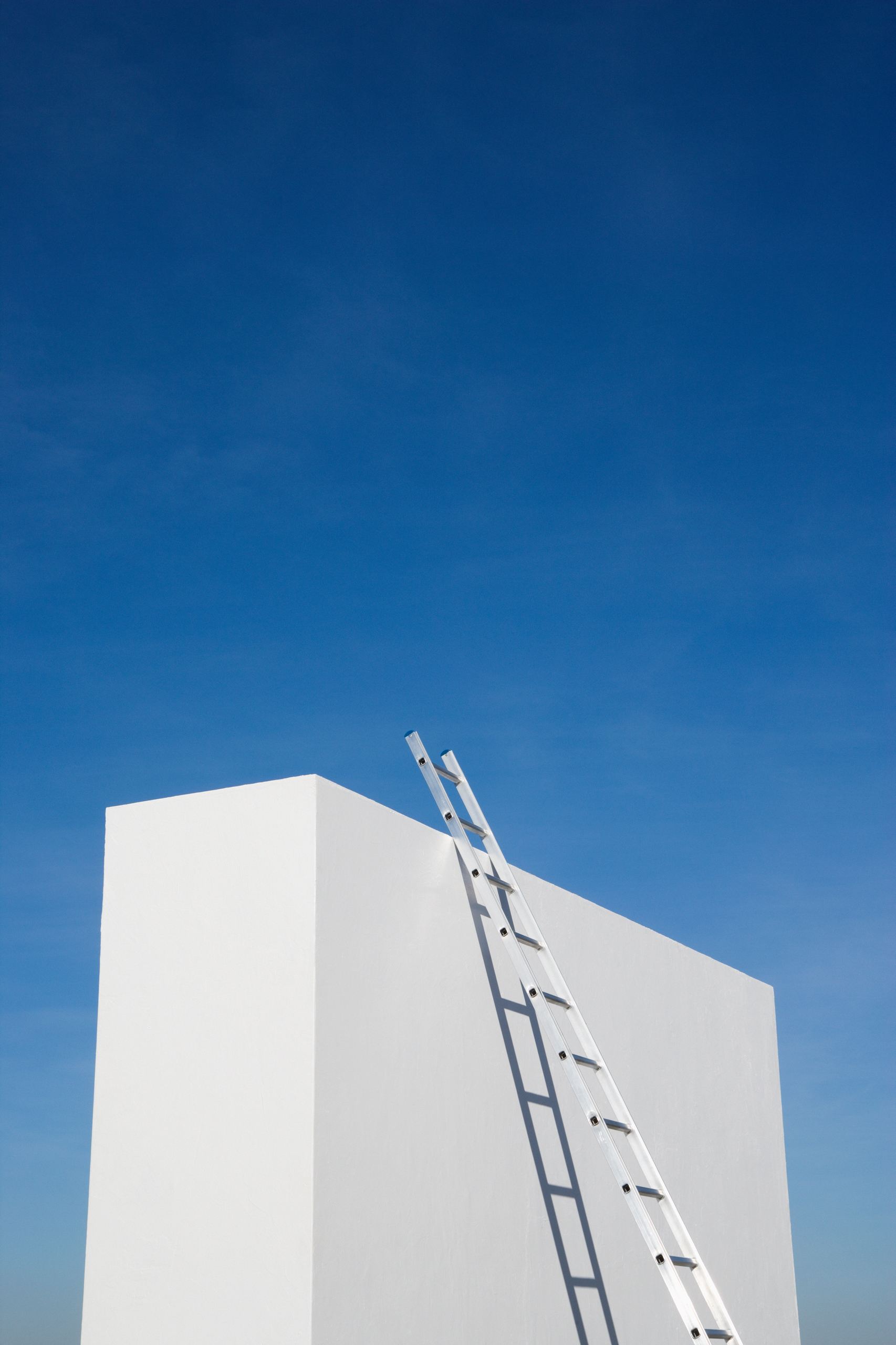 White ladder extending above a small white tower into a bright blue sky, symbolizing a ladder to success.