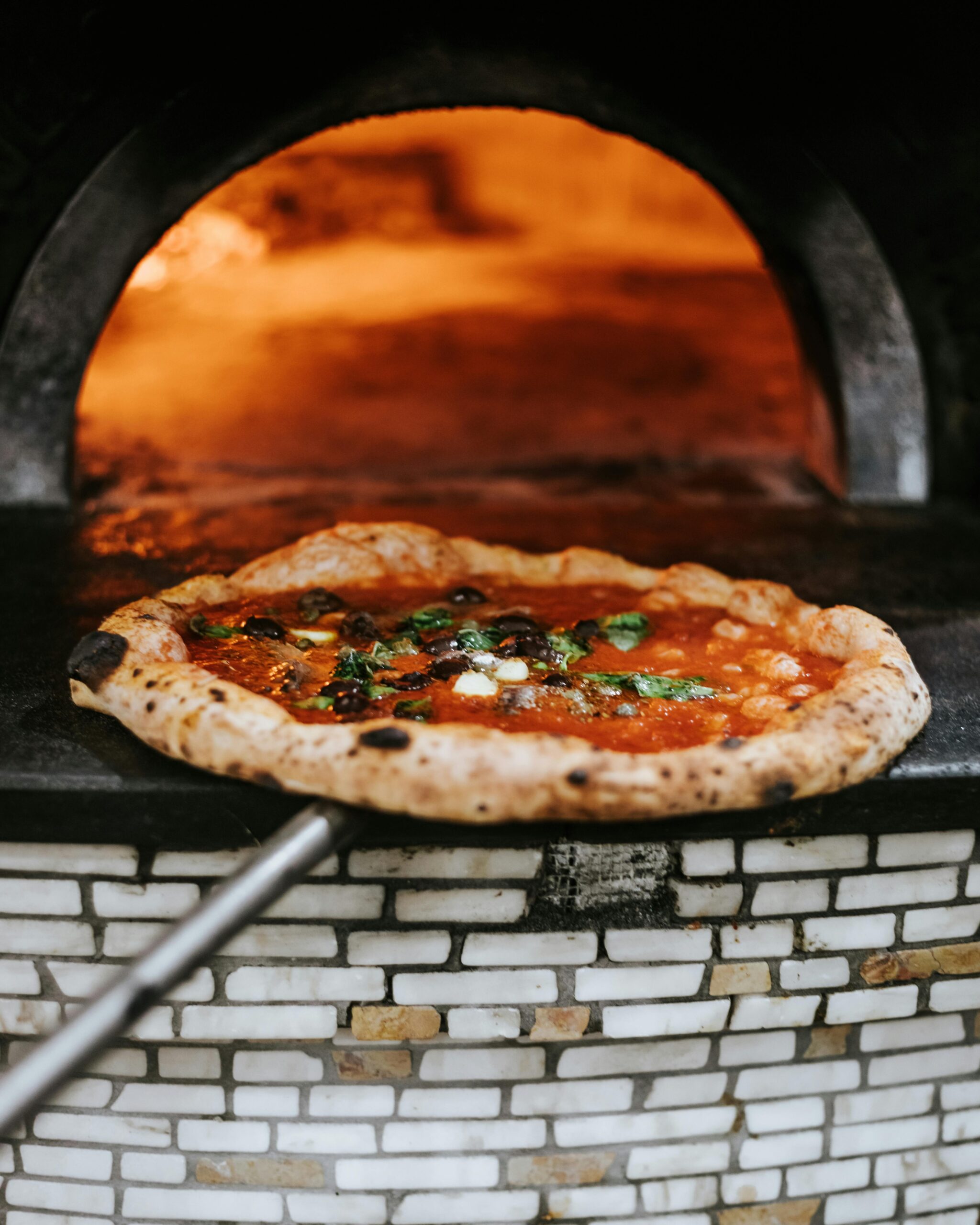 Uncooked pizza topped with fresh ingredients placed on a peel, ready to slide into a traditional pizza oven at Patti’s Pizzeria.